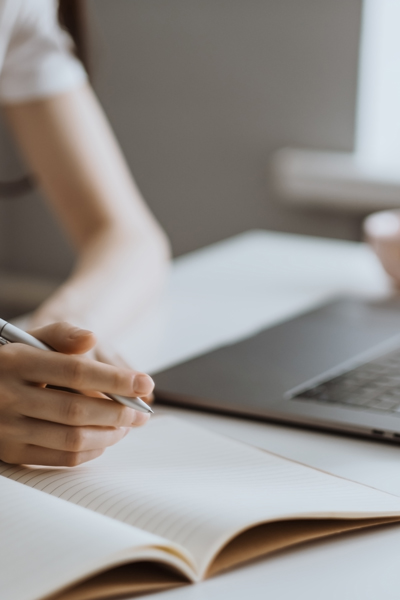 a person writing in a notebook with a pen while using a laptop for learning or studying productivity